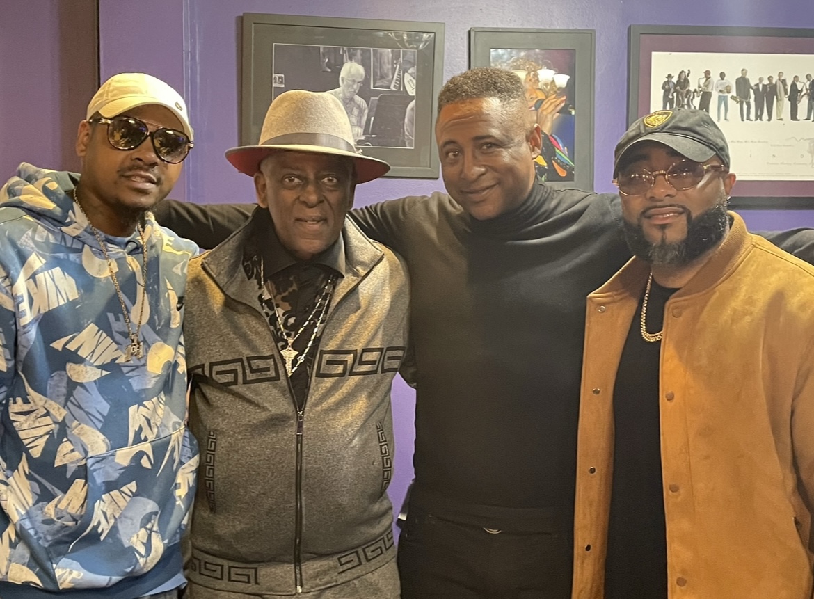 Fast Freddy Anderson in a grey track set and wide brim hat with three friends inside a Detroit lounge.
