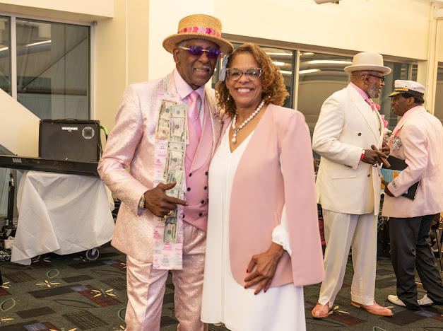 Fast Freddy Anderson with dollar bills pinned to his pink suit, posing with a guest. 80th birthday celebration.