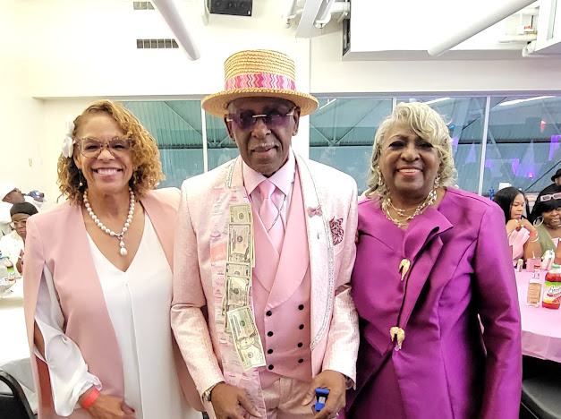 Fast Freddy Anderson in his pink suit and boater hat with two guests dressed in pink and purple. 80th birthday celebration.