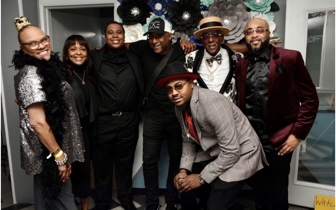 Fast Freddy Anderson celebrating with a group of friends and family in front of a paper flower wall.