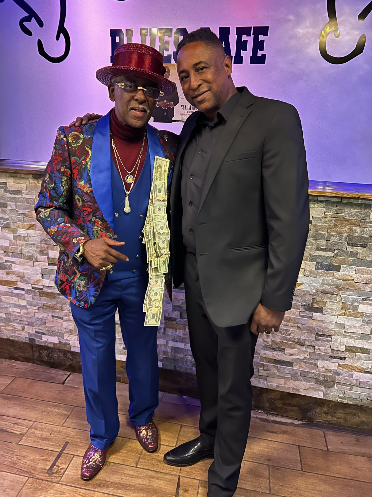 Fast Freddy Anderson in a royal blue and floral suit with a money tie posing with a guest at the Blues Cafe.
