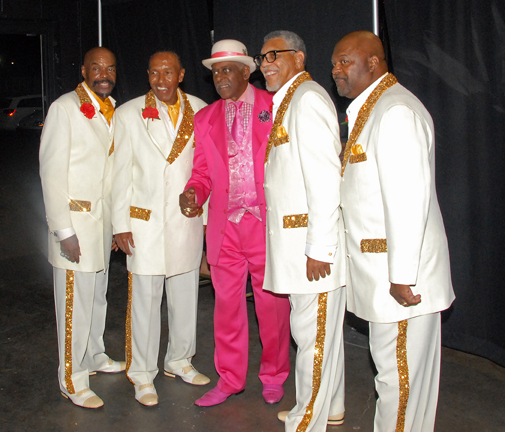 Fast Freddy in a hot pink suit celebrating backstage with a vocal group