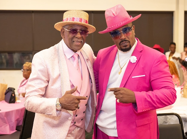 Fast Freddy Anderson pointing playfully alongside a guest in a hot pink suit and pink hat. 80th birthday celebration.