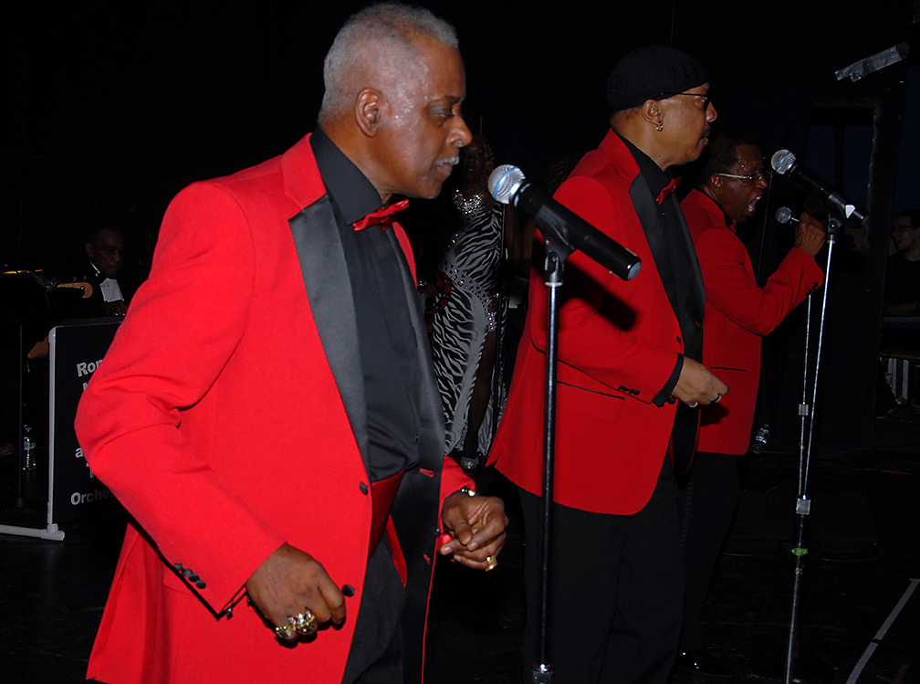 Fast Freddy performing on stage in a red tuxedo jacket with a live band