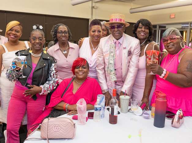 Fast Freddy Anderson with a large group of guests in pink gathered around a party table. 80th birthday celebration.