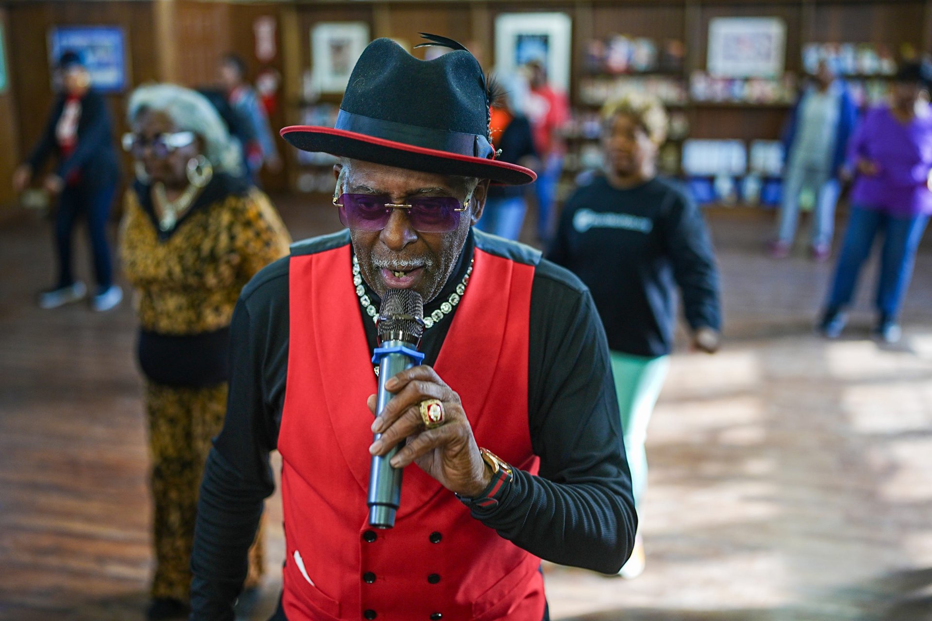 Fast Freddy singing into the microphone in a red vest and black hat